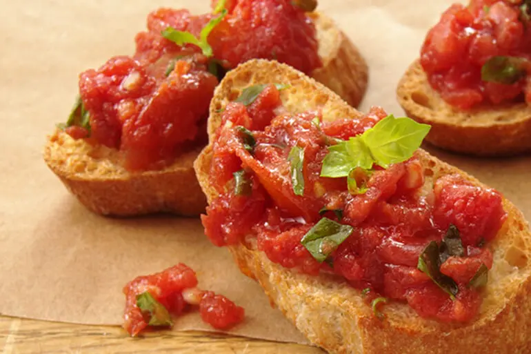 Bruschetta with diced tomatoes and basil recipe served on a wooden chopping board.